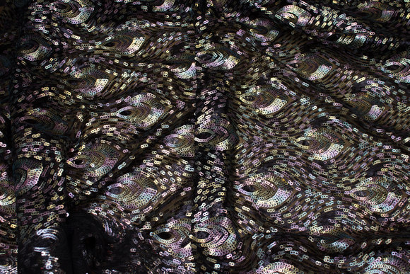 Flot pailletstof med påfuglemønster på sort bund af mesh